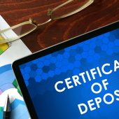 Certificate of Deposit (CD) in white type on blue background shown on tablet on desk with eyeglasses, pen and a colorful chart