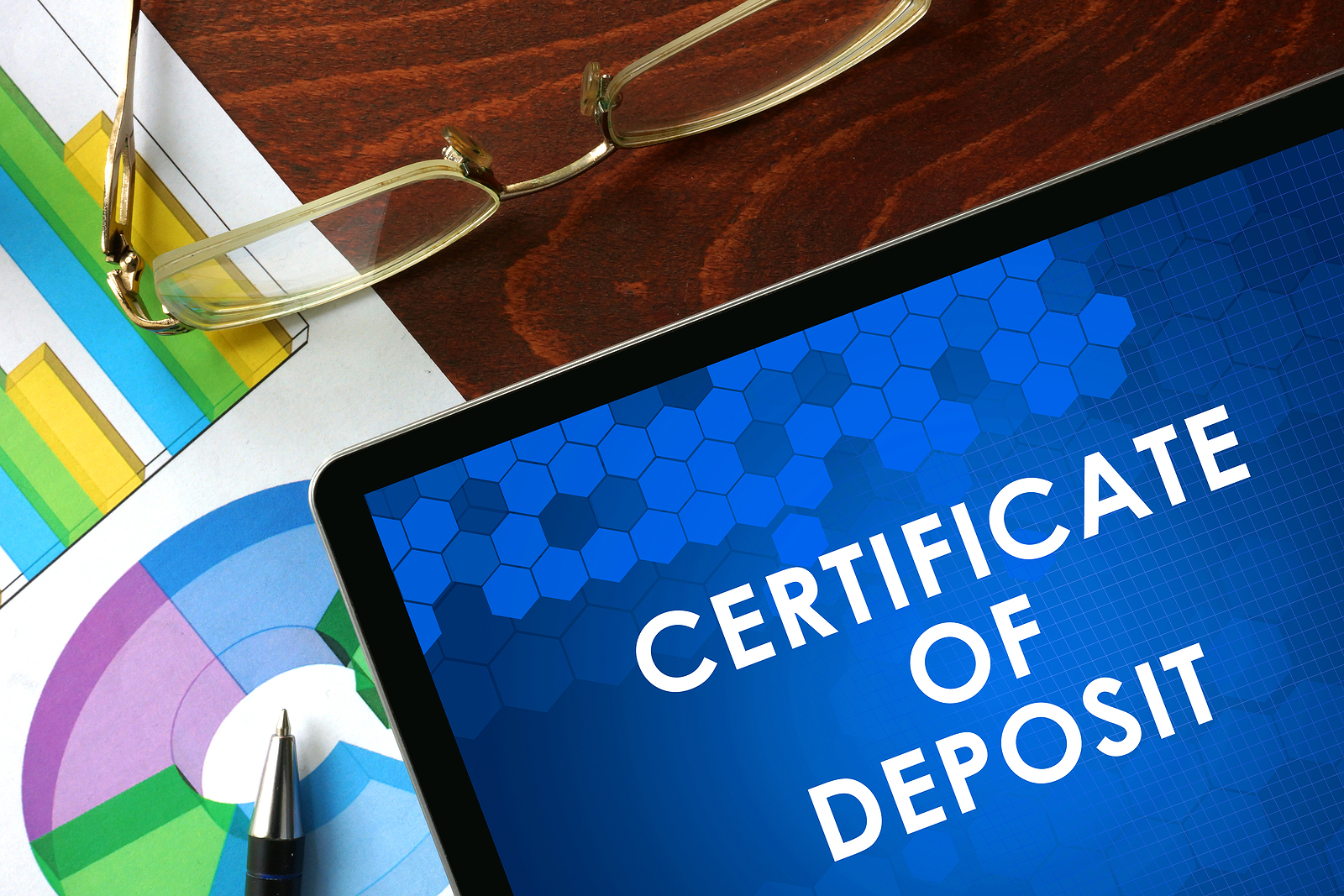 Certificate of Deposit (CD) in white type on blue background shown on tablet on desk with eyeglasses, pen and a colorful chart